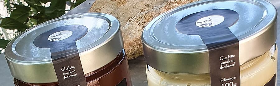 Die Deckel zweier Honiggläser mit rundem Siegel und dem Hinweis, das Glas an den Imker zurückzugeben.